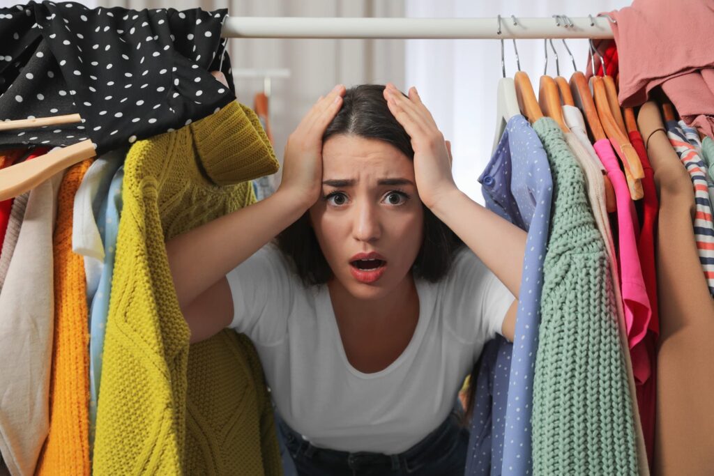 Overwhelmed woman with hands on head looking through a rack of clothes in her closet